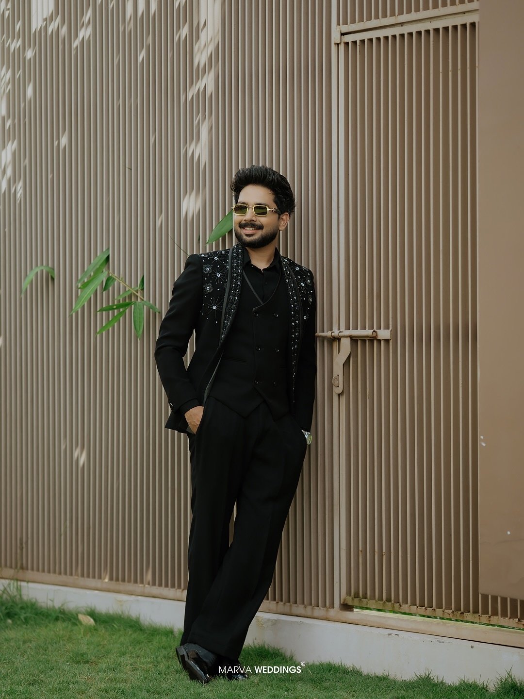 Groom posing in a black suit beside an architectural screen