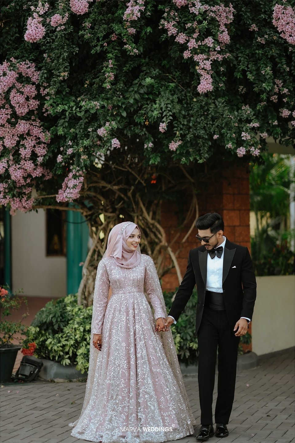 Newlyweds walking hand in hand beneath flowering branches